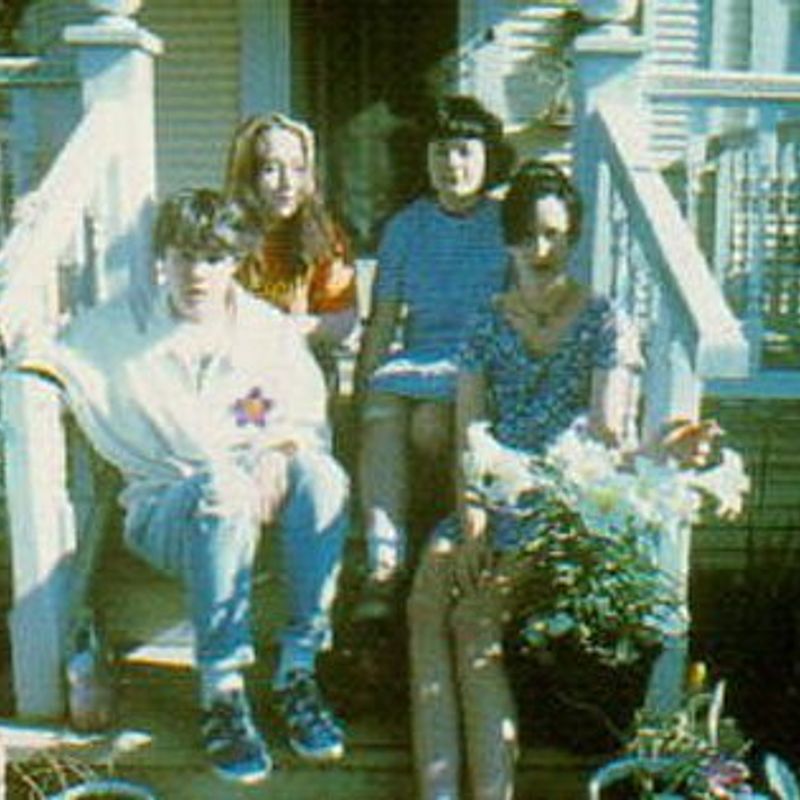 A low fidelity digital file of a colour film photograph depicting 4 teenagers (the band Tiger Trap) sat on the front steps outside a suburban house. Probably in Sacramento.